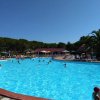 Piscina all'aperto con persone che nuotano, circondata da lettini e ombrelloni.