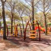 Parco giochi tra gli alberi, con strutture colorate per arrampicarsi e scivoli.