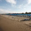 Spiaggia sabbiosa con file di sdraio e ombrelloni blu.