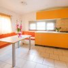 Cucina luminosa con mobili arancioni, tavolo bianco e sedute. Fiori sul tavolo.