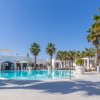 Piscina circondata da palme e lettini, cielo sereno, architettura mediterranea.