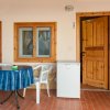 Veranda con tavolo, sedie di plastica, frigo bianco e porta aperta in legno.