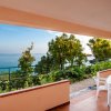 Una veranda con tavolo e sedie bianche, vista sul mare e vegetazione.