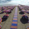 Spiaggia con file ordinate di ombrelloni e lettini colorati.