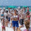 Persone partecipano a una festa in spiaggia con schiuma, molte sorridenti e coperte di bolle.