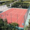 Campo sportivo recintato con superficie rossa, circondato da alberi e aree verdi.