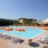 Ampia piscina con ombrelloni gialli e arancioni. Lettini disposti ordinatamente intorno.
