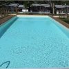 Una piscina all'aperto con acqua limpida, circondata da un'area con sdraio e alberi.