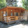 Casetta in legno con veranda, sedie bianche e circondata da alberi.