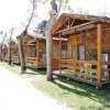 Serie di bungalow di legno con portici e sedie bianche su un prato.