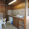 Cucina in legno con lavello, frigorifero e fornello. Tavolo con sedie bianche.