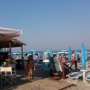 Una spiaggia affollata con ombrelloni blu e un chiosco con sedie da esterno.