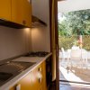 Cucina con mobili gialli, lavello, piano cottura e vista su un balcone con tavolo e sedie bianche.