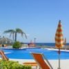 Piscina all'aperto con ombrellone arancione, vista mare e palme.