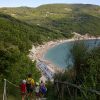 Sentiero verso una spiaggia con persone, collina e mare.