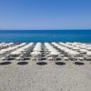 Spiaggia con file di ombrelloni bianchi e mare blu.