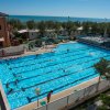 Piscina all'aperto con nuotatori e vista mare.