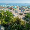 Spiaggia con ombrelloni a strisce e piante tropicali.