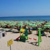 Spiaggia affollata con ombrelloni verdi e gialli, area giochi per bambini e mare sullo sfondo.