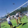 Ragazzi giocano a pallavolo su un campo erboso sotto un cielo sereno.