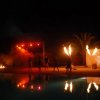 Spettacolo notturno con effetti di fuoco e luci rosse, palme sullo sfondo.