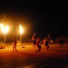 Artisti eseguono uno spettacolo di fuoco di notte, con pubblico sullo sfondo.
