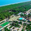 Vista aerea di un villaggio turistico con piscine, campi sportivi e una foresta vicino al mare.