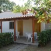 Una casetta bianca con veranda e tavolo, circondata da cespugli e alberi.