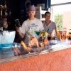 Due persone dietro un bancone con fiamme sulla superficie e cocktail colorati in primo piano.