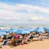Spiaggia affollata con ombrelloni blu e lettini, vicino al mare calmo sotto un cielo nuvoloso.