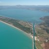Vista aerea di un canale che collega un lago al mare con terreni e colline circostanti.