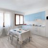 Cucina moderna con mobiletti azzurri, tavolo apparecchiato e finestre con tende bianche.