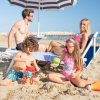 Famiglia in spiaggia, genitori su sdraio, bambini giocano con la sabbia.